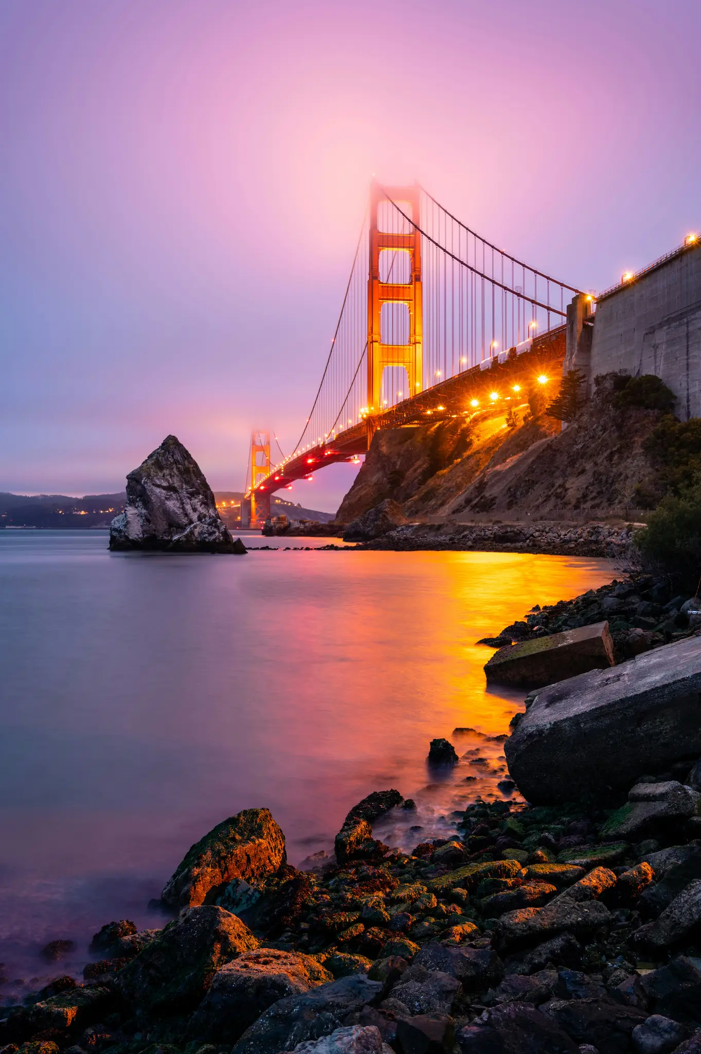Dlouhoexponovaná fotografie mostu Golden Gate za soumraku nebo úsvitu s jeho oranžovými věžemi a světly odrážejícími se na…