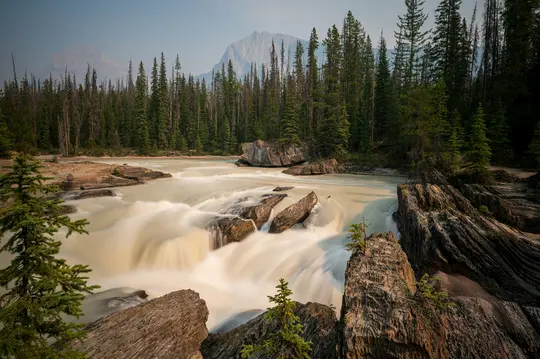 Een lange belichtingsopname van een rivier met romig witte stroomversnellingen die over donkere rotsen stromen, omringd door