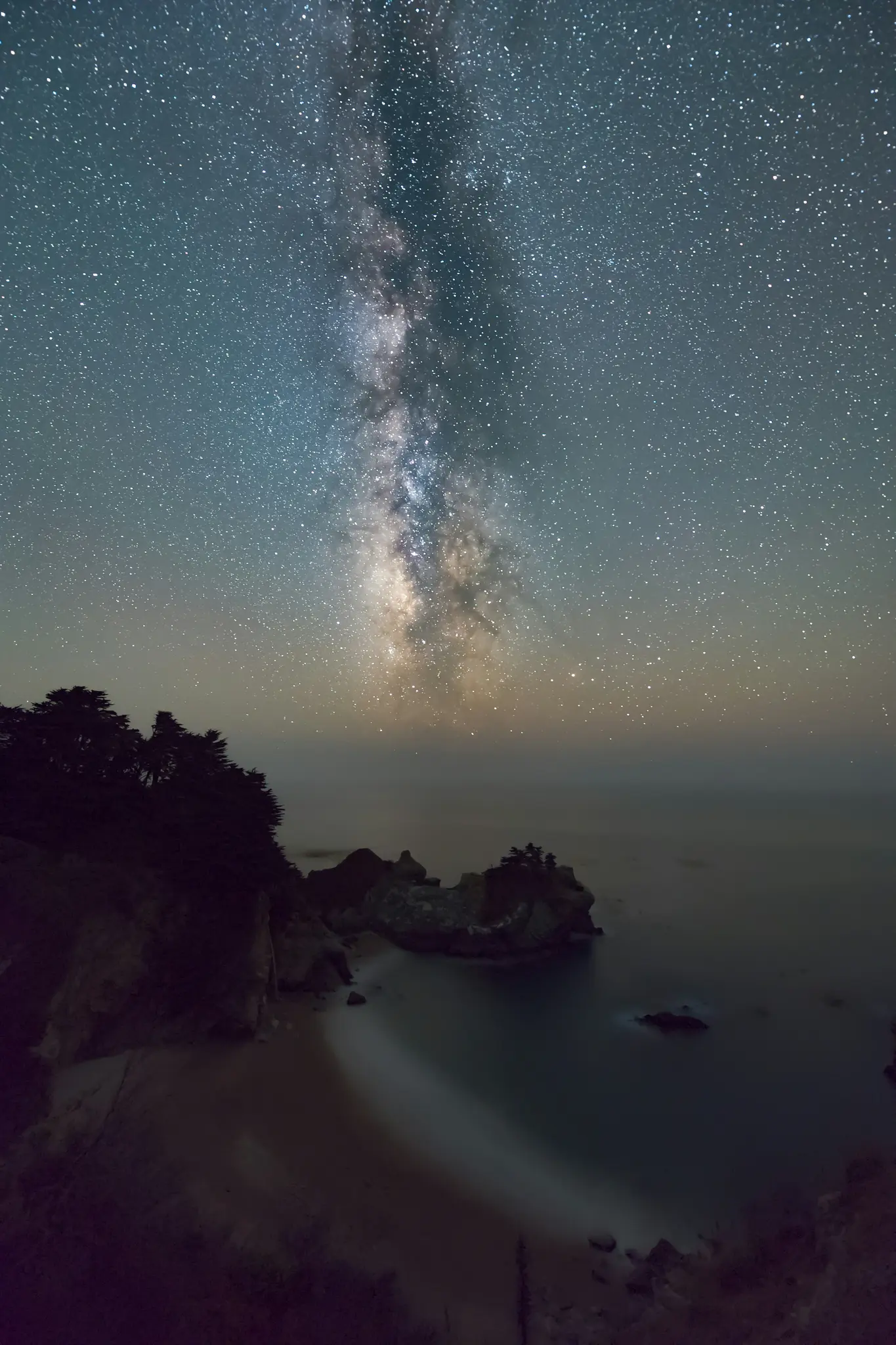 Een adembenemend nachtlandschap toont de Melkweg die zich boven een afgelegen strand en de oceaan uitstrekt.