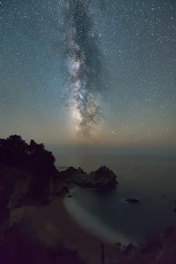 Een adembenemend nachtlandschap toont de Melkweg die zich boven een afgelegen strand en de oceaan uitstrekt.