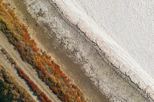 En flygfotografering från hög vinkel av ett kargt landskap. Bilden är diagonalt uppdelad i tre huvudsektioner: rödbruna...