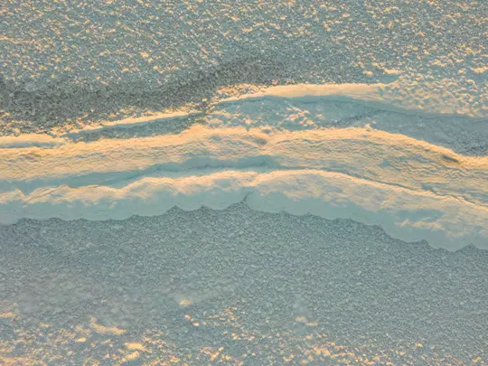 Una vista aérea abstracta de una superficie helada texturizada con líneas onduladas de nieve y hielo, iluminada por una