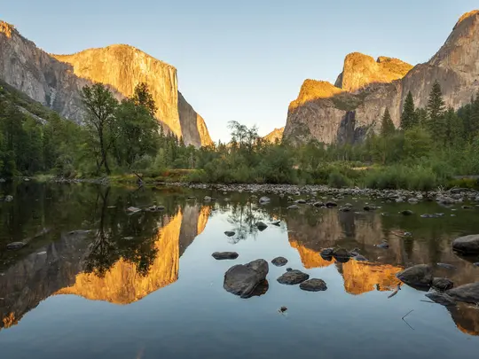 Een brede landschapsfoto van Yosemite Valley. Een rustige rivier op de voorgrond weerspiegelt zonovergoten granieten kliffen