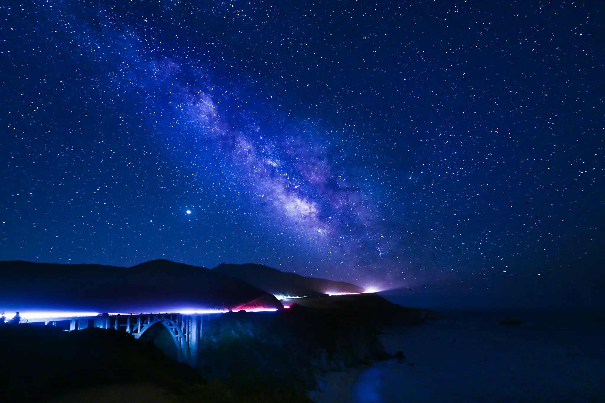Una fotografia notturna a lunga esposizione mostra la Via Lattea che si estende su un cielo blu scuro sopra il ponte Bixby e