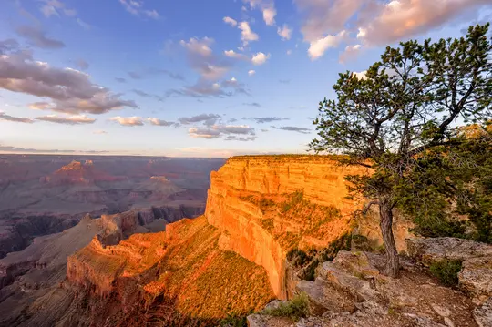 Een brede landschapsfoto van de Grand Canyon bij zonsondergang, met uitgestrekte oranje en rode rotsformaties onder een