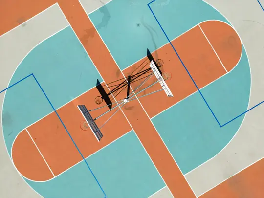 Una vista aérea, de arriba abajo, de una vibrante cancha de baloncesto exterior pintada en naranja, azul claro y gris.