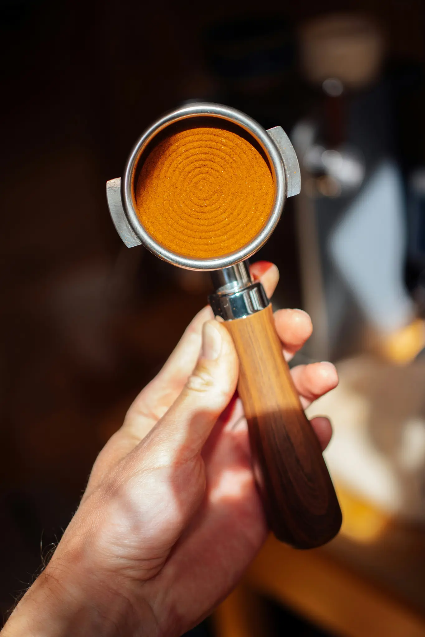 A close-up shot of a hand holding a portafilter filled with finely ground coffee, featuring concentric circles on its…