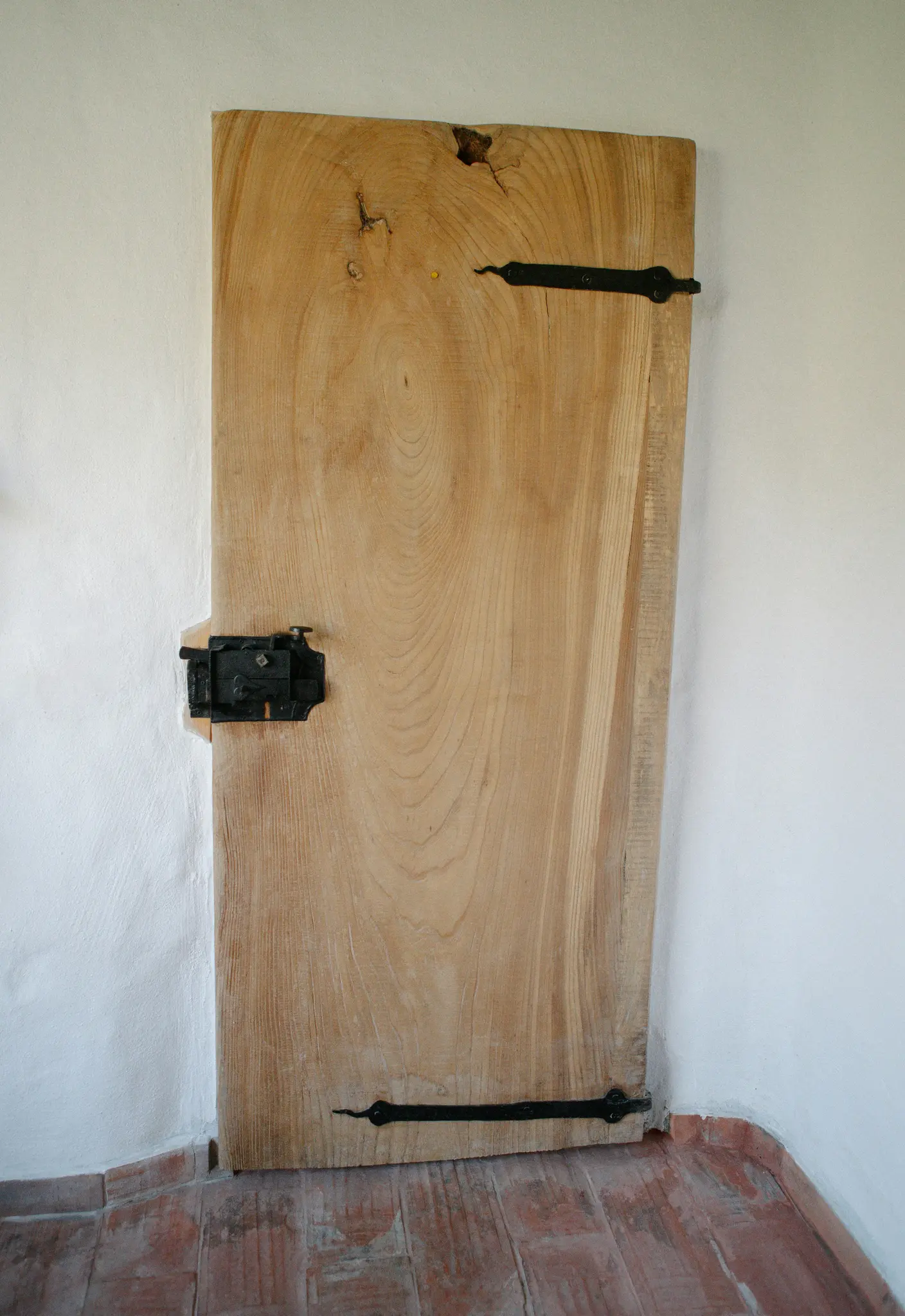 Een opname van een rustieke, lichtgekleurde houten deur met zichtbare nerf en knoesten, met zwarte metalen scharnieren en...