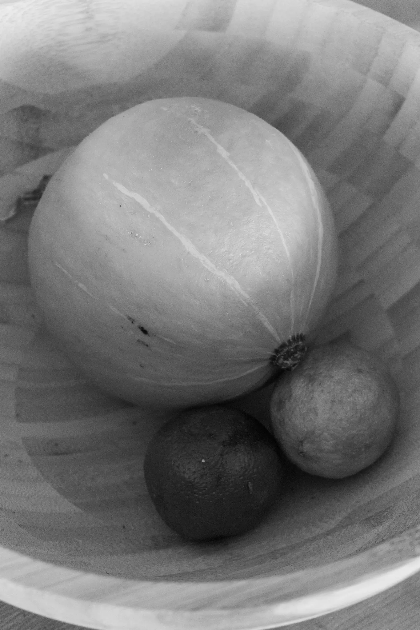 Un gros plan en noir et blanc vu de dessus montre un grand melon de couleur claire et deux agrumes plus petits et plus foncés