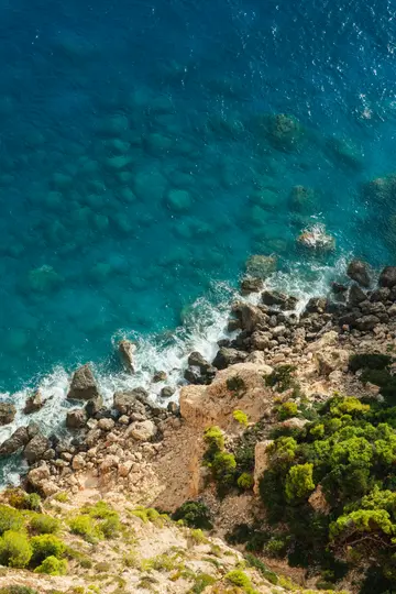 Una vista aérea muestra vibrantes aguas turquesas del océano que se encuentran con una escarpada costa rocosa. Las olas