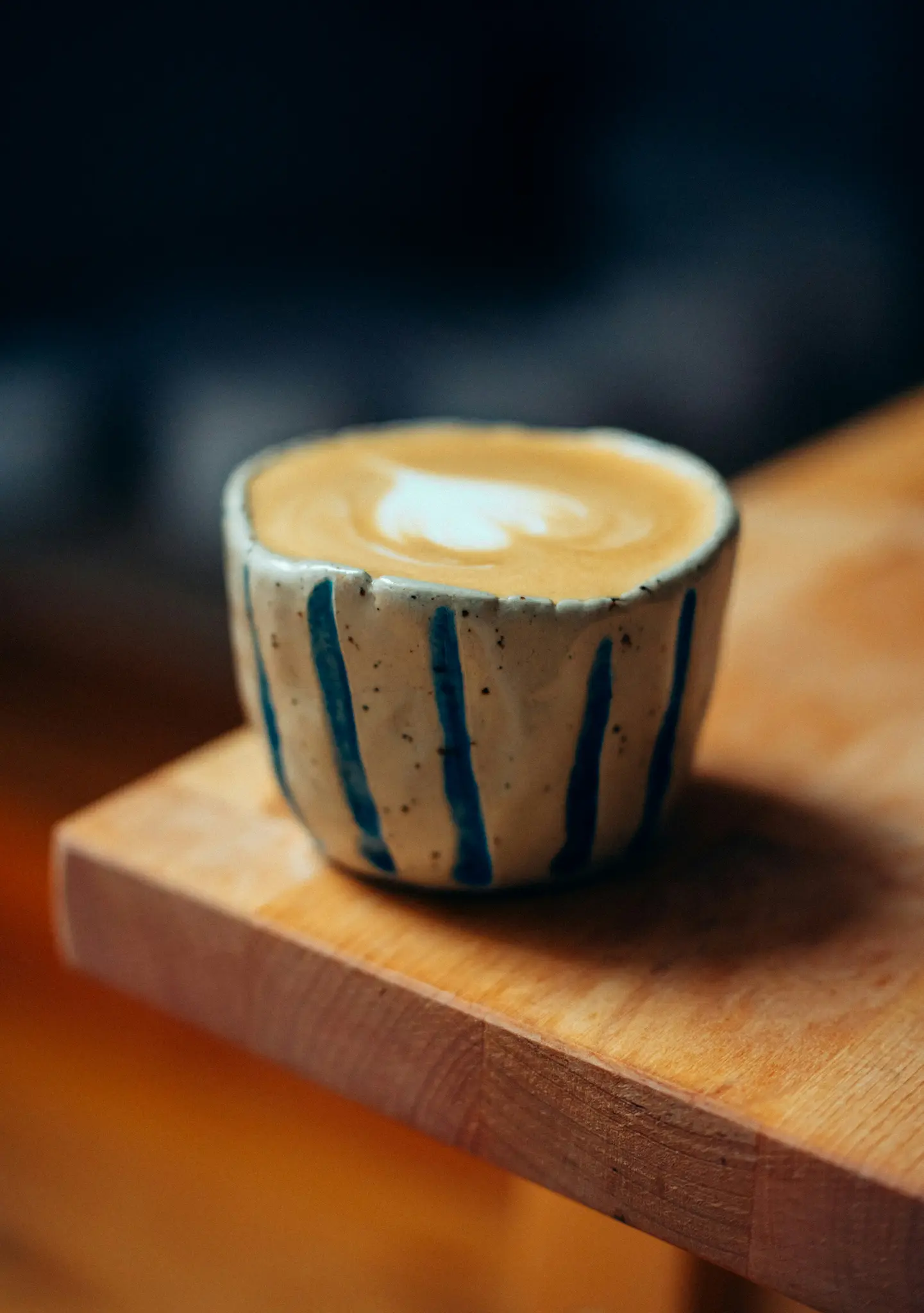 Gros plan d'une tasse en céramique à rayures verticales bleues, contenant un latte avec un motif de mousse en forme de cœur