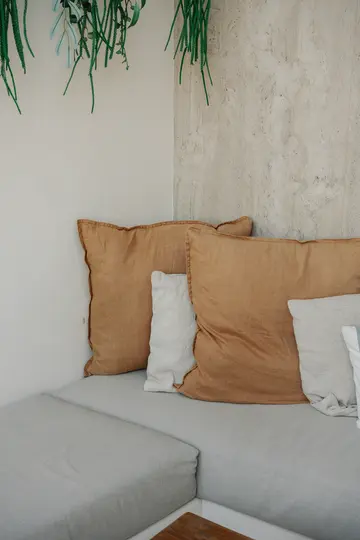 Un acogedor rincón cuenta con cojines gris claro, dos grandes de color óxido y dos más pequeños blancos.