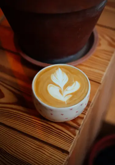 Una tazza di ceramica bianca con piccoli punti rossi contiene un latte con un'intricata arte di schiuma bianca simile a una