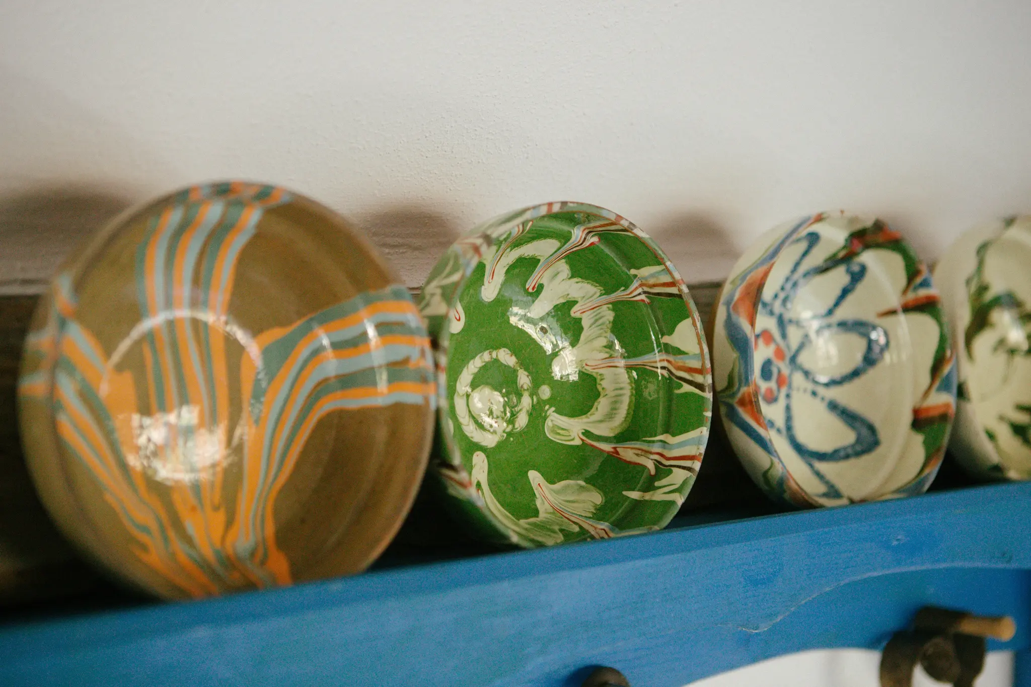 Vier keramische schalen met ingewikkelde patronen staan op een doorleefde blauwe houten plank tegen een lichte muur. Patronen