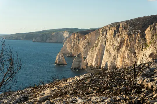 Une vue panoramique d'une côte accidentée avec de hautes falaises claires rencontrant une mer bleu profond. Deux stacks