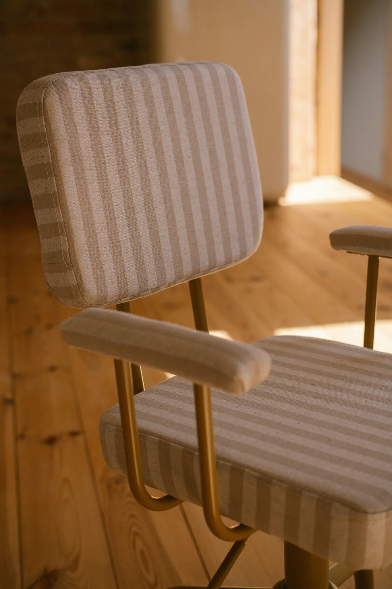 Närbild av en modern kontorsstol med beige och ljusbrunt randigt tygklädsel och en gyllene metallram.