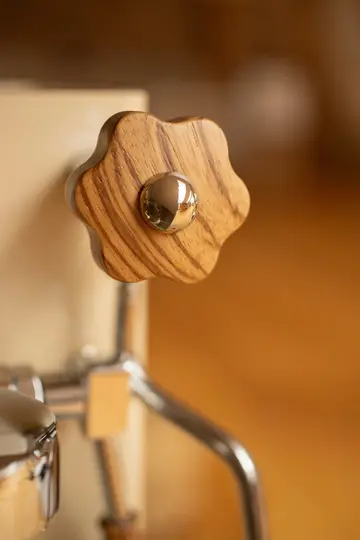 Een close-up van een stervormige houten knop met een chromen bolvormig middenstuk, bevestigd aan een machine.