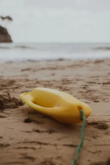 Un tubo de rescate amarillo brillante con una cuerda verde descansa sobre la arena mojada de una playa. Las olas del océano