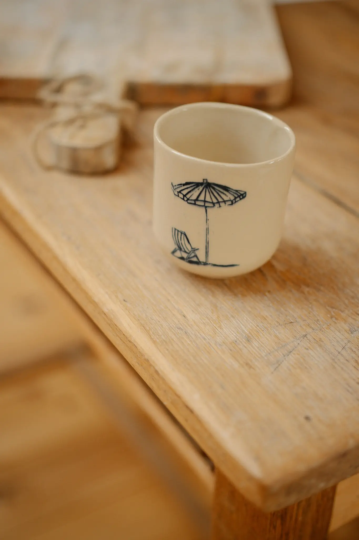 Une tasse en céramique de couleur crème avec une illustration bleue d'un parasol de plage et d'une chaise longue est assise