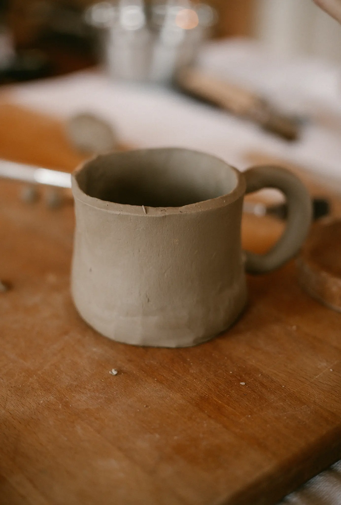 Nahaufnahme einer hellbraunen, unglasierten Tonne Tasse mit Henkel, die auf einem warmfarbigen Holzschneidebrett steht.