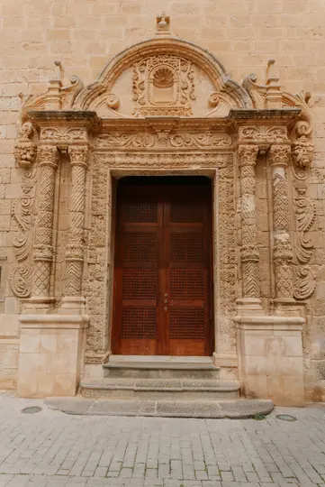 Vista dettagliata di un elaborato portale in pietra con intagli intricati, colonne e una doppia porta in legno marrone scuro.