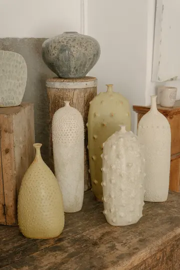 Una composizione di natura morta di vari vasi in ceramica testurizzata in tenui tonalità di verde, grigio e bianco sporco su