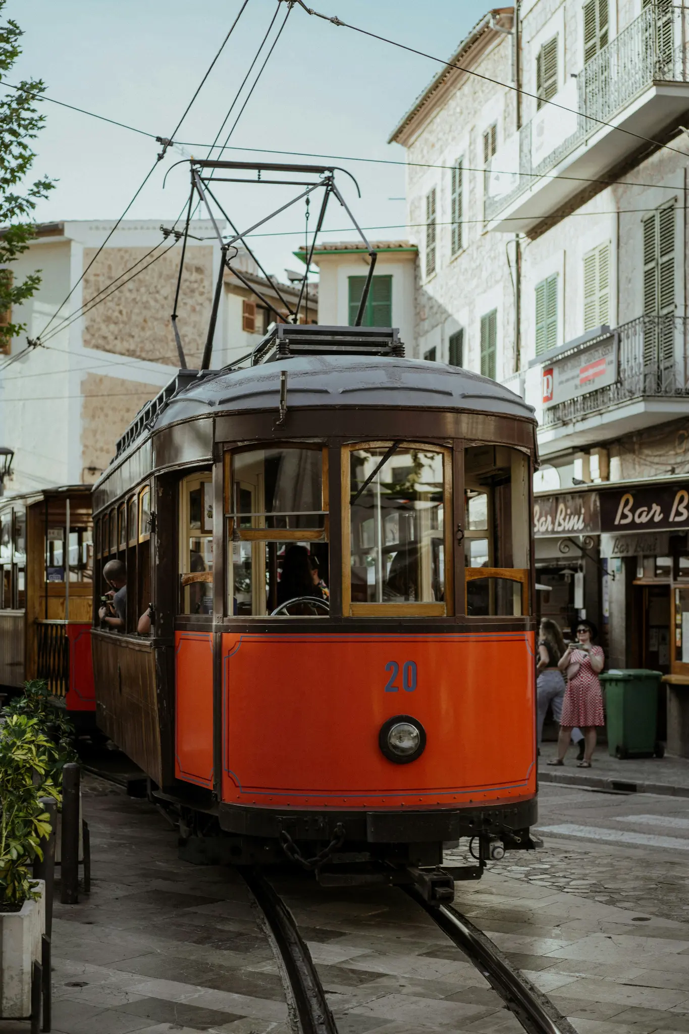 Eine alte orange-braune Straßenbahn mit der Nummer 20 steht auf Schienen in einer europäischen Stadtstraße mit Steingebäuden.