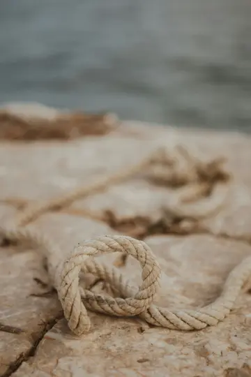 Λήψη από κοντά στο ύψος των ματιών ενός παχιού, ανοιχτόχρωμου σχοινιού τυλιγμένου σε μια ανάγλυφη, ανοιχτό καφέ πέτρινη