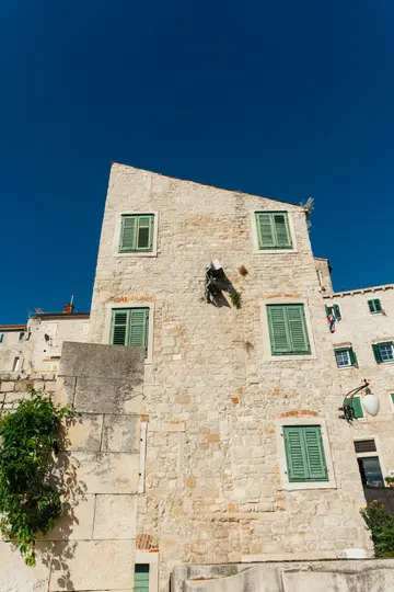 Une prise de vue en contre-plongée d'un ancien bâtiment en pierre avec plusieurs fenêtres, chacune équipée de volets verts en