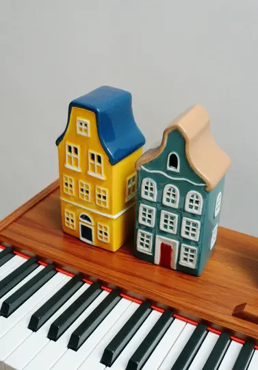 Two colorful ceramic house figurines, one yellow with a blue roof and one teal with a beige roof, sit on a wooden surface…