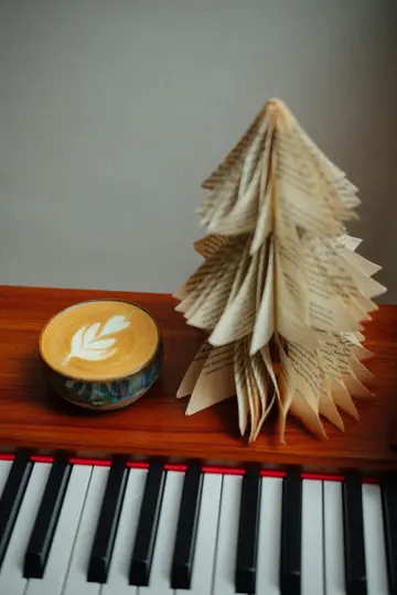 Una tazza di ceramica di latte con un disegno a foglia nella schiuma si trova accanto a un albero di Natale fatto di pagine