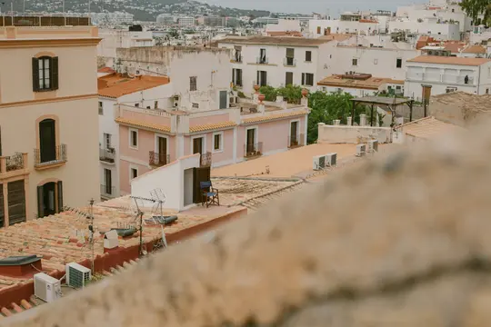 Una vista elevata di una città mediterranea con numerosi edifici con tetti in terracotta e facciate bianche, beige…