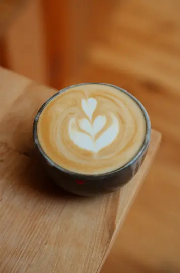 A close-up, high-angle shot of a ceramic cup filled with latte, featuring intricate heart-shaped latte art.