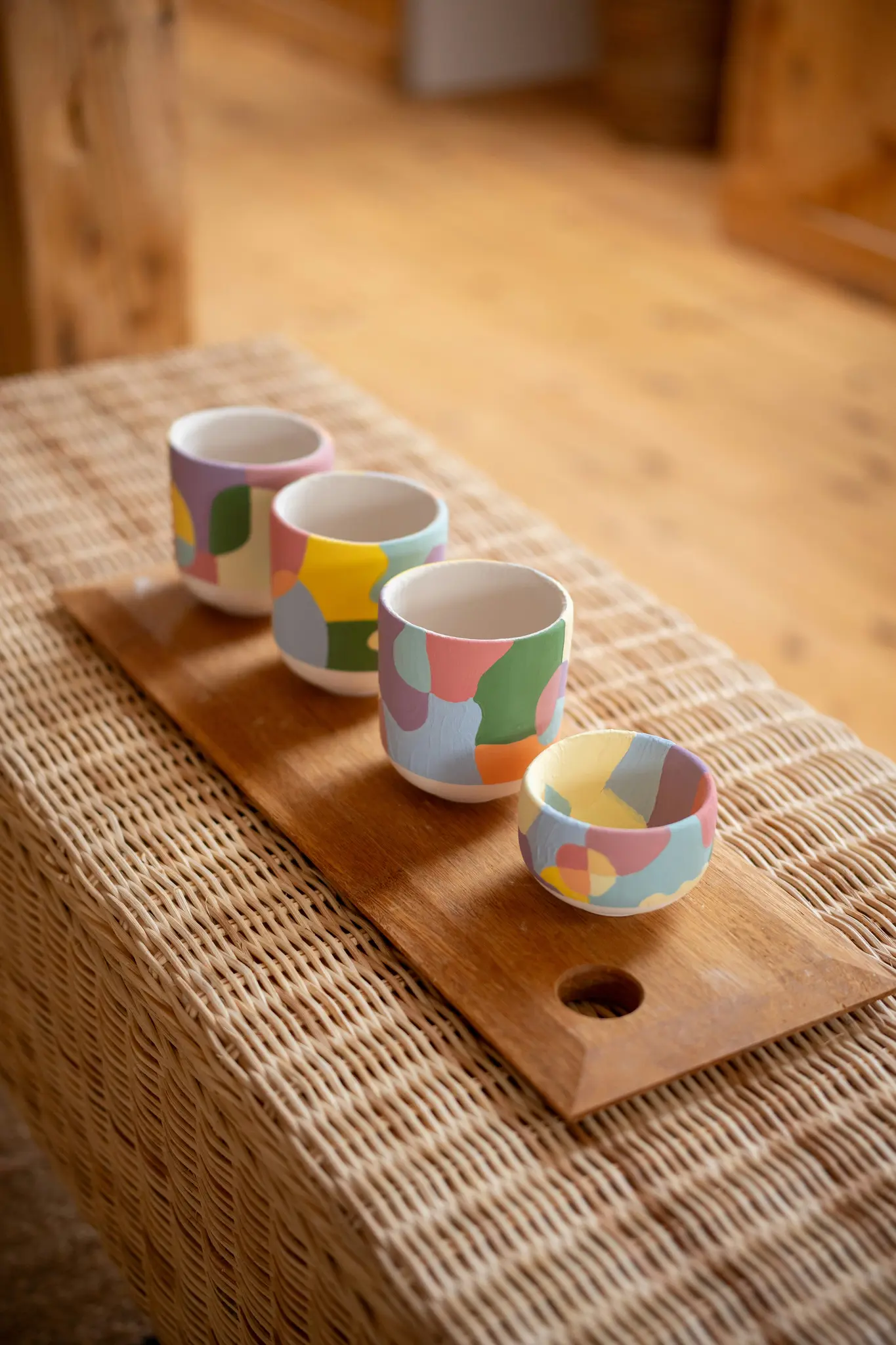 Quatre tasses en céramique, chacune ornée de motifs abstraits uniques aux couleurs pastel, sont présentées sur une planche en