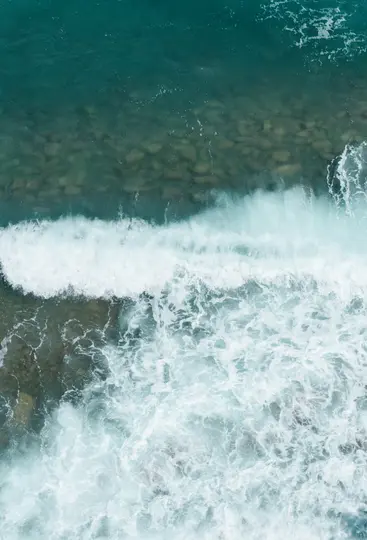 Μια εναέρια λήψη από ψηλά με τιρκουάζ νερά ωκεανού με λευκά αφρώδη κύματα που σκάνε πάνω σε βυθισμένους καφέ βράχους.