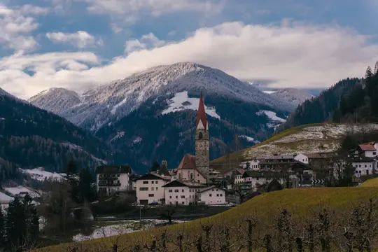 Un village pittoresque avec un haut clocher et un toit rouge se trouve dans une vallée, entouré de montagnes enneigées et…