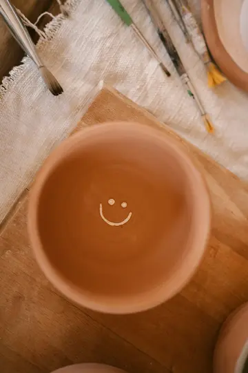 Un primo piano dall'alto di una ciotola in terracotta con una faccina sorridente bianca disegnata a mano all'interno.