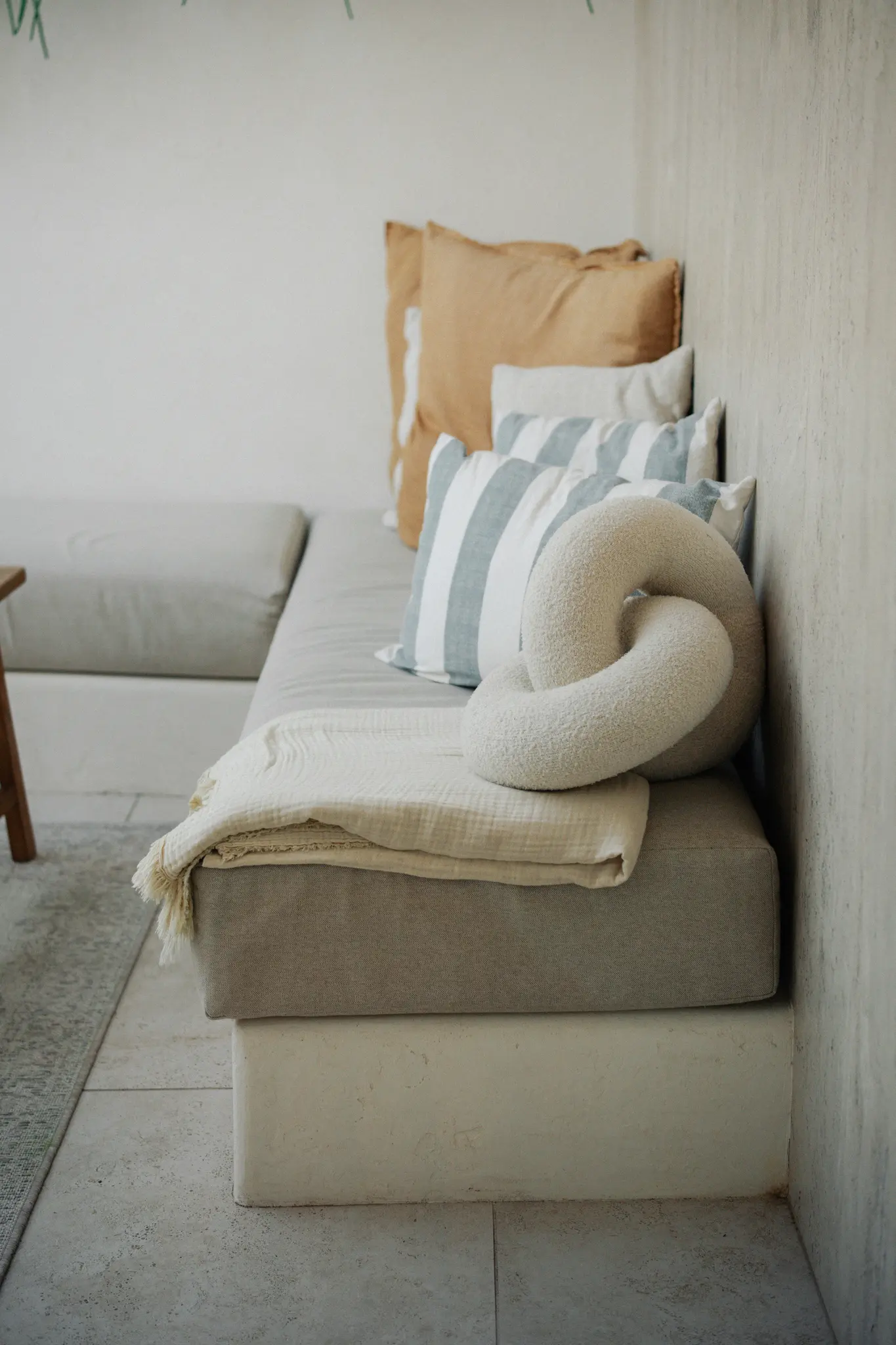 Wbudowana sofa z jasnoszarymi poduszkami, ozdobiona beżowym kocem i zestawem poduszek.