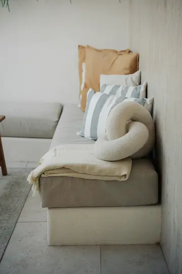 Un sofá empotrado con cojines de color gris claro, adornado con una manta beige y una variedad de cojines.