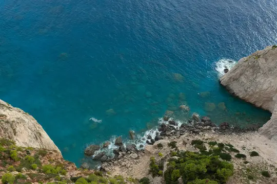 Una toma aérea que mira hacia abajo a una costa accidentada donde acantilados de color gris claro se encuentran con el océano