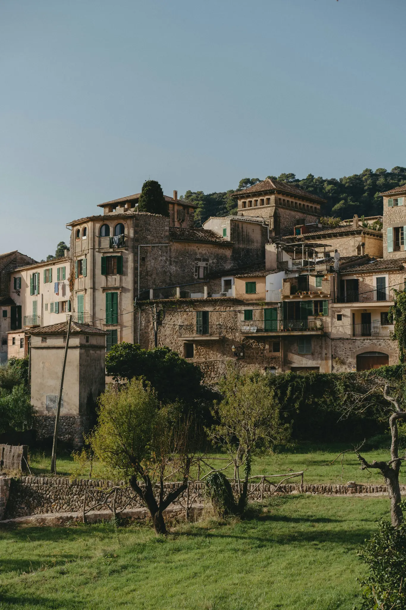 Eine malerische Aussicht auf ein Dorf am Hang mit traditionellen Steingebäuden und grünen Fensterläden, vor einem Hintergrund