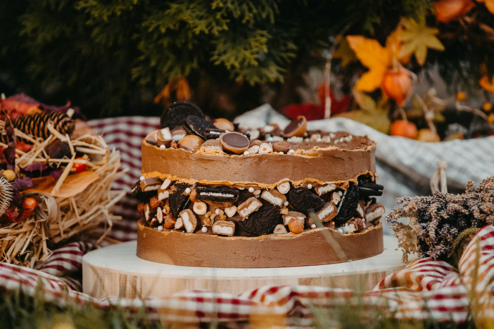 Een rijke chocoladetaart, versierd met chocoladeglazuur, koekjes, snoepjes en hazelnoten, staat op een houten standaard