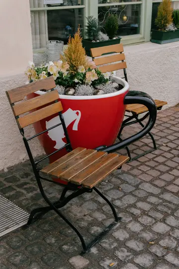 A large red coffee cup planter with a white silhouette of a woman's head and a pitcher, filled with plants and flowers.