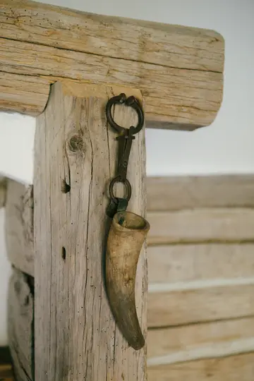 Een close-up van een lichtbruine drinkhoorn met een donkere metalen sluiting, hangend aan een verweerde houten balk.