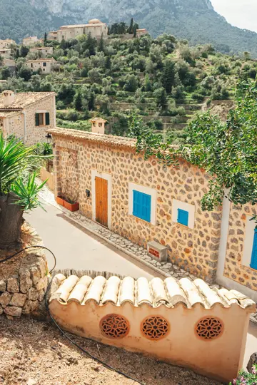 Una casa in pietra con porta in legno e persiane blu brillante in una strada stretta. Pendii terrazzati e montagne sullo