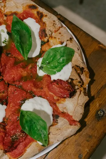 Detailní pohled shora na pizzu s tlustým, lehce připáleným okrajem. Je pokryta jasně červenou rajčatovou omáčkou, kousky...
