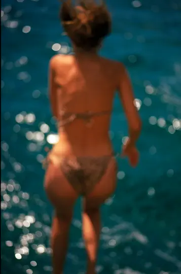 O imagine încețoșată, neclară, arată spatele unei persoane într-un costum de baie cu imprimeu leopard, stând în fața unui