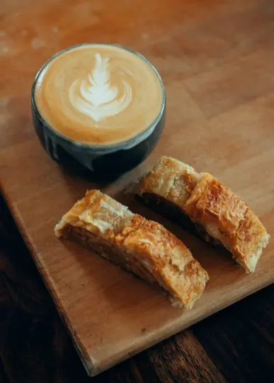 Una tazza grigia scura di latte con arte latte bianca è seduta su un tagliere di legno marrone chiaro accanto a due