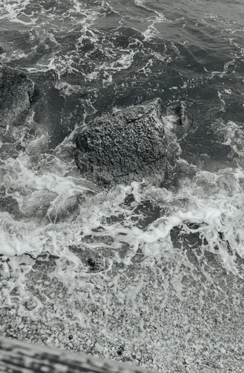 Primo piano in bianco e nero da una prospettiva aerea di onde oceaniche con schiuma bianca che si infrangono su rocce scure e