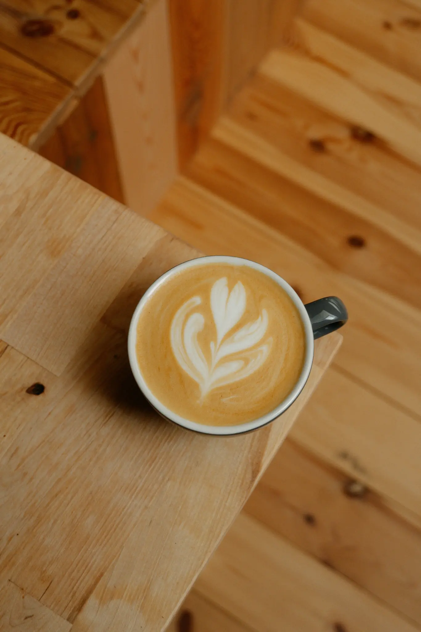 Gros plan d'un latte dans une tasse gris foncé, avec un art latte blanc complexe sur une surface brun clair, vu de dessus.